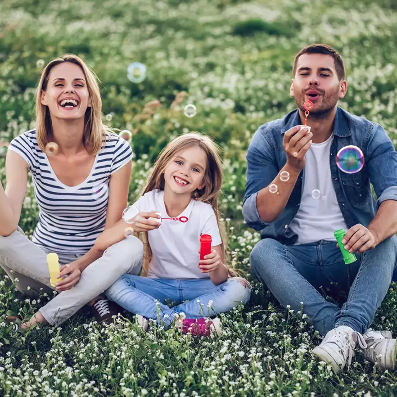 A family sit together in the grass and blow bubbles.