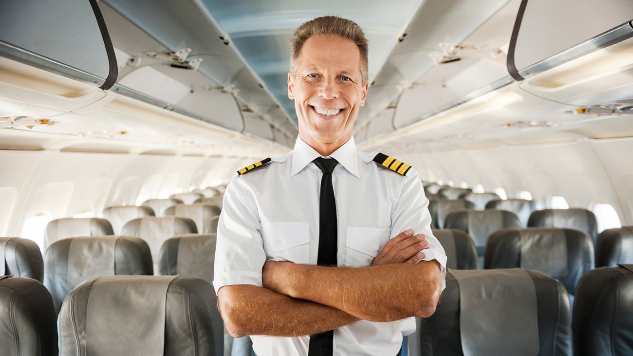 A male airline pilot smiling confidently in the aisle of an empty airplane