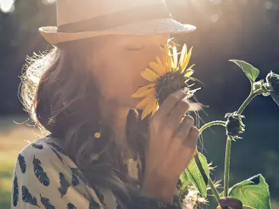 A woman stands in a field and smells a sunflower.