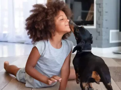 A little girl sits and the floor and plays with her dog.