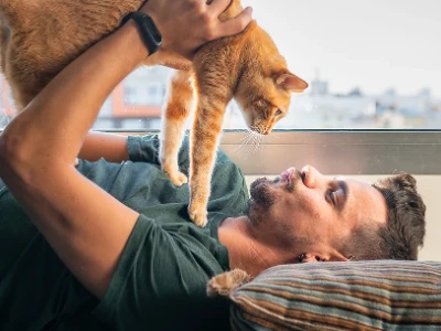 A young man lying in bed, playing with his cat.