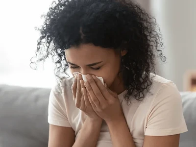 Mujer sentada en el sofá mientras se suena la nariz.