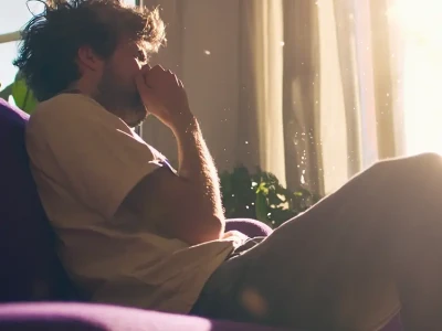 Mulher sentada no sofá assoando o nariz.