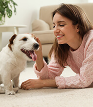 Jonge vrouw ligt op de grond in de woonkamer en aait haar hond.