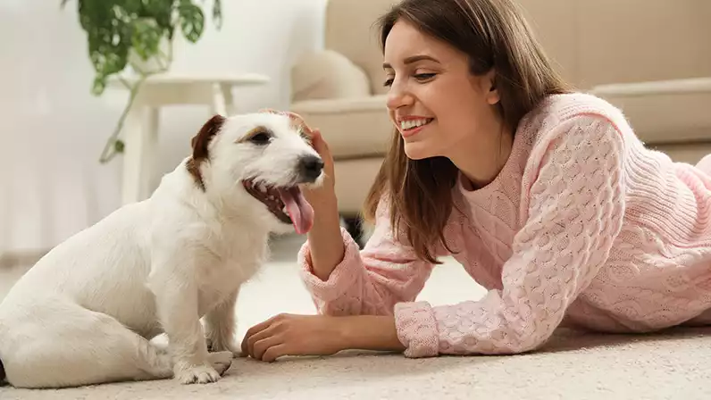 A woman sits on the floor next to her dog.
