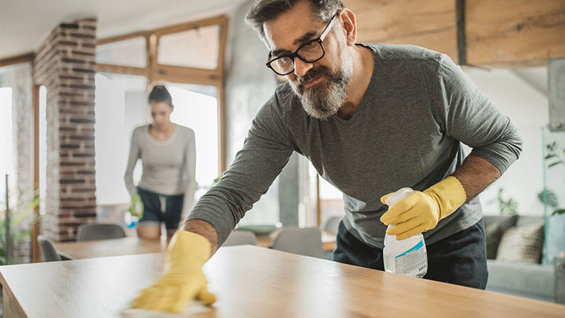 A woman wearing plastic gloves, cleans her counter tops.