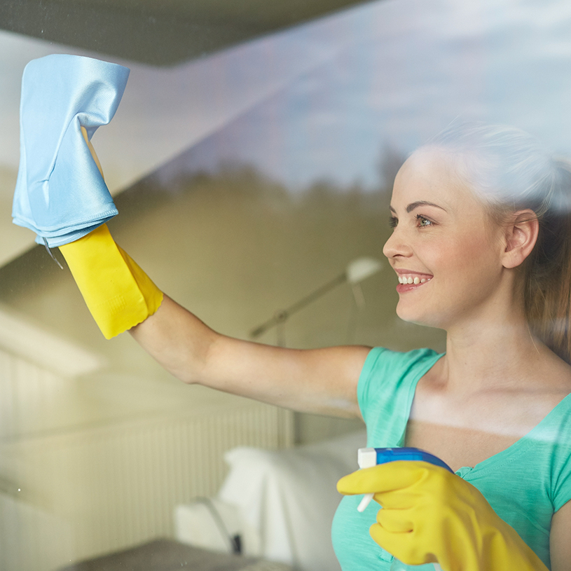 Eine Frau putzt ihre Fenster von innen und trägt dabei Gummihandschuhe.