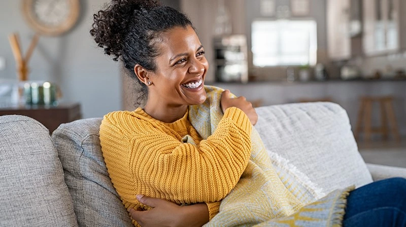 Vrouw zit lachend op de bank met een deken omgeslagen