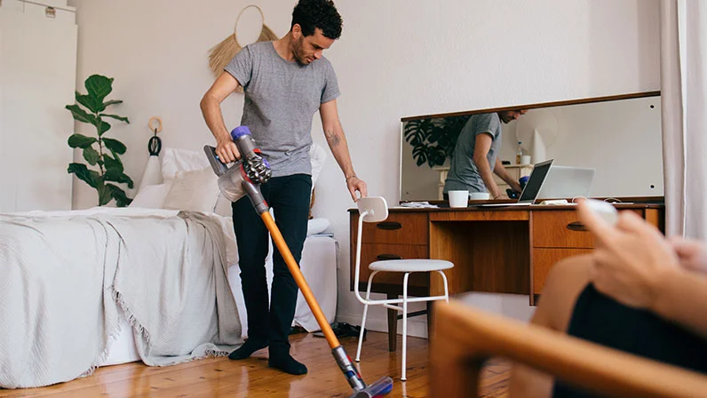 Een man stofzuigt zijn woonkamer en schuift de stoel aan de kant