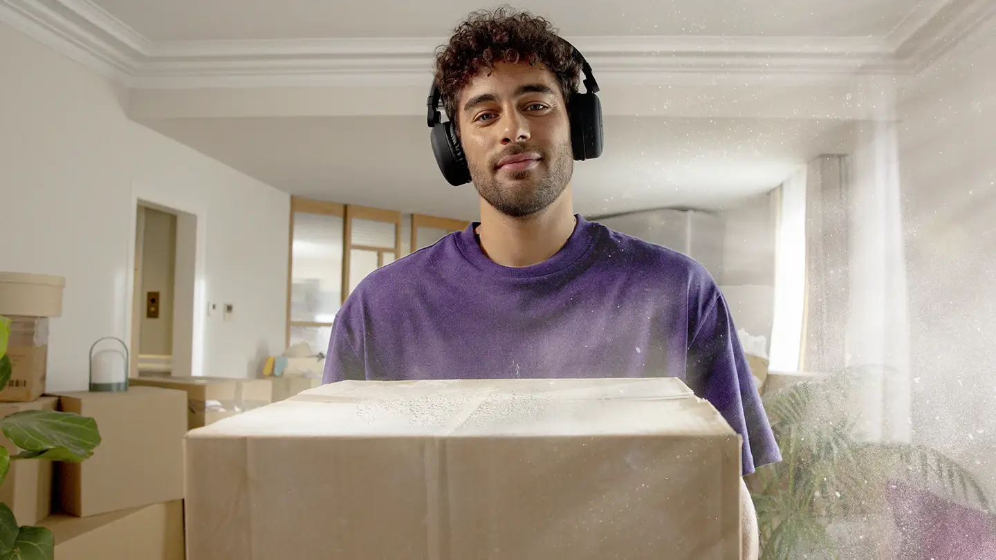 A man standing in a living room, holding a moving box, with dust particles in the air.