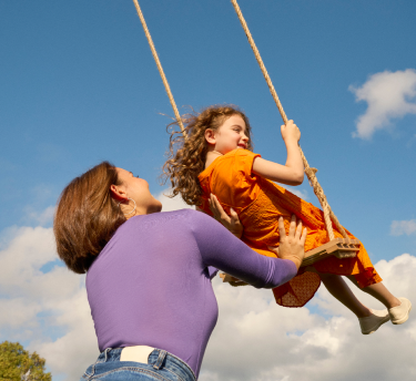 A happy girl swings high on a rope swing as her mother looks on, enjoying an allergy free sunny day outdoors.