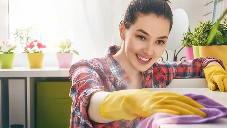La femme polit le dessus d'un placard avec un chiffon violet.